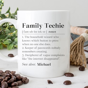 May include: White ceramic mug with the text "Family Techie" and its definition. The definition includes the role of a household wizard and keeper of passwords. The mug is surrounded by coffee beans and decorative items.