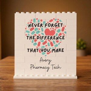 May include: A white building block display sign featuring a heart shape composed of small red and teal pill illustrations. The text reads: NEVER FORGET THE DIFFERENCE THAT YOU MAKE, followed by the personalized name Avery Pharmacy Tech in black.