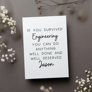 May include: A white greeting card with black text that reads "If you survived Engineering you can do anything. Well done and well deserved Jason." The card is surrounded by white flowers and sprigs on a gray background.