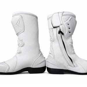 Puede incluir: Par de botas de moto blancas con suelas negras. Las botas tienen un diseño alto y protector con paneles reforzados, cierre de cremallera y zona de puntera texturizada. Las botas están diseñadas para la seguridad y el rendimiento.