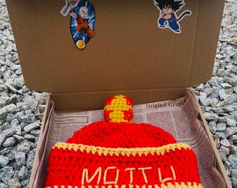 May include: Red and yellow crocheted beanie with the word "MOTT" embroidered on the front. The beanie is in a cardboard box with a brown paper lining.
