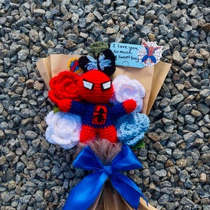 May include: A crocheted bouquet featuring a red and blue Spiderman character, white and blue crocheted flowers, and a blue ribbon. The bouquet is wrapped in brown paper and includes a card that says "I love you so much my sweet boy".