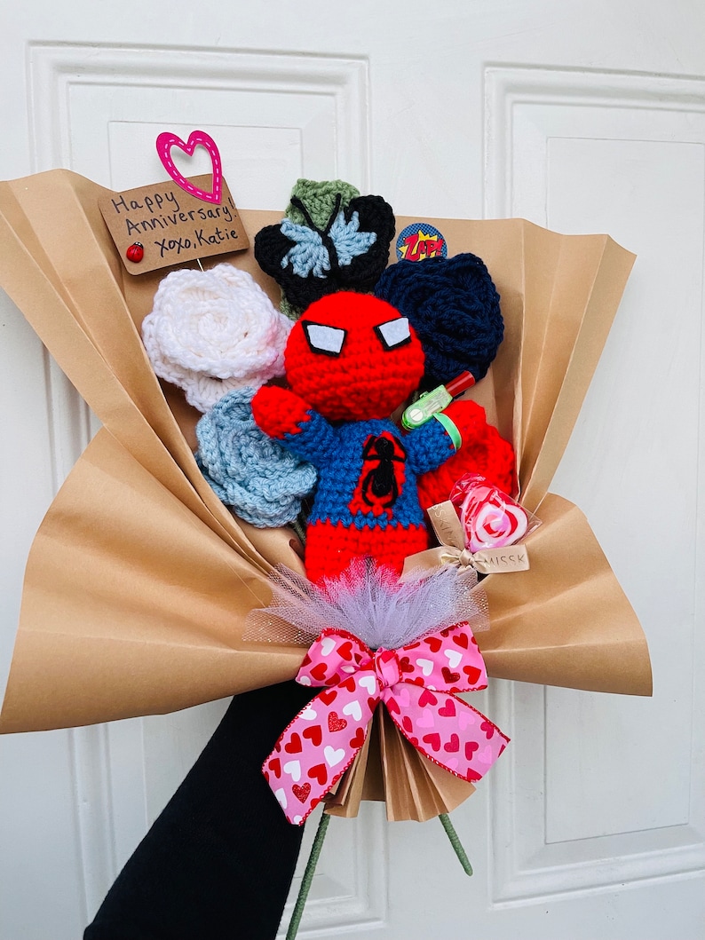 May include: A brown paper bouquet with a crocheted Spiderman figure, a pink bow with white hearts, and a card that says "Happy Anniversary! xoxo Katie".