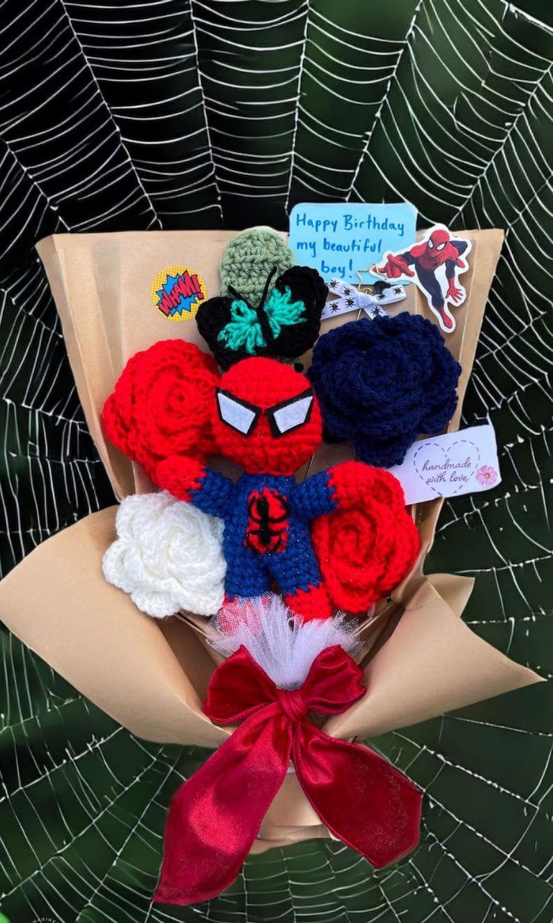 May include: A crocheted bouquet featuring a Spiderman character, red and white roses, a blue rose, a green butterfly, and a red bow. The bouquet is wrapped in brown paper and has a tag that says "handmade with love". The bouquet also includes a card that says "Happy Birthday my beautiful boy!"
