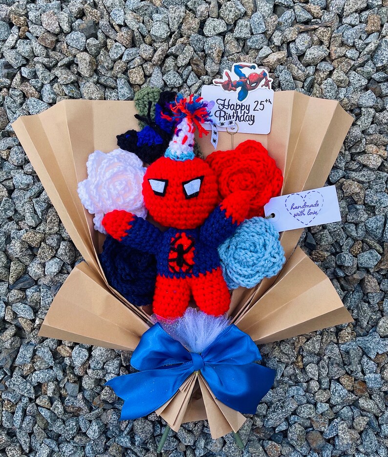 May include: A crocheted bouquet featuring a red and blue Spiderman character, white, red, and blue flowers, and a card that says "Happy 25th Birthday".