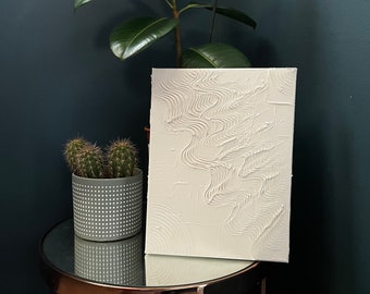 May include: White abstract painting with raised lines and circles on a canvas. The painting is on a small round table with a mirrored top.