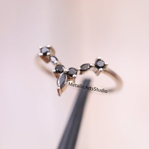 Pode incluir: Um anel de prata com um design delicado com cinco pedras preciosas pretas. O anel está sobre um fundo preto.