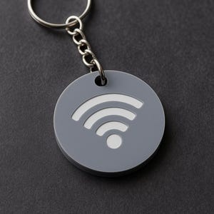 May include: A grey, circular keyring featuring a white Wi-Fi symbol. It has a silver chain and ring. The background is a dark grey surface.