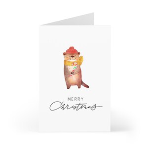 May include: A Christmas card featuring a cartoon otter wearing a red hat and yellow scarf, holding a candy cane. The card reads "Merry Christmas".
