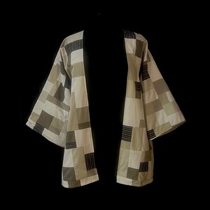 Puede incluir: Chaqueta estilo kimono patchwork en tonos neutros de beige, verde oliva y gris. La chaqueta presenta un patrón geométrico de cuadrados y rectángulos. El diseño abierto y las mangas anchas crean una silueta relajada.