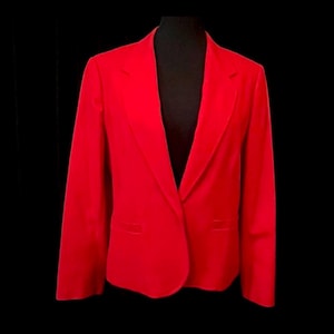Op de afbeelding: Een felrode blazer, gepresenteerd op een zwarte mannequin. De blazer heeft een klassieke revers, twee voorzakken en een sluiting met één knoop. De getailleerde pasvorm en de opvallende kleur maken het een statement-stuk.
