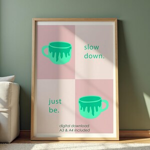 Könnte beinhalten: Ein gerahmter Kunstdruck mit einem hellen Holzrahmen. Der Druck zeigt eine türkisfarbene Kaffeetasse in zwei Ecken mit den Worten "slow down." und "just be." in Türkis. Der untere Teil des Drucks lautet "digitaler Download A3 & A4 enthalten".