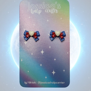 May include: A pair of blue and red bow earrings with a white heart in the center. The earrings are displayed on a card with the text "jossica's half center" and "ig/tiktok: @jossicashalfcenter".