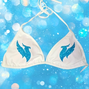 Peut inclure: Un haut de bikini blanc avec un lien &agrave; nouer autour du cou et deux bonnets triangulaires. Chaque bonnet est orn&eacute; d'un motif &agrave; paillettes bleu vif repr&eacute;sentant un oiseau stylis&eacute; aux ailes d&eacute;ploy&eacute;es, plac&eacute; sym&eacute;triquement sur le devant.