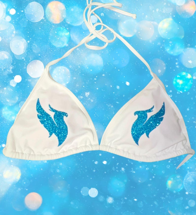 Peut inclure: Un haut de bikini blanc avec un lien &agrave; nouer autour du cou et deux bonnets triangulaires. Chaque bonnet est orn&eacute; d'un motif &agrave; paillettes bleu vif repr&eacute;sentant un oiseau stylis&eacute; aux ailes d&eacute;ploy&eacute;es, plac&eacute; sym&eacute;triquement sur le devant.