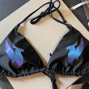 Peut inclure: Un haut de bikini noir orn&eacute; d'un motif de ph&eacute;nix en d&eacute;grad&eacute; bleu et violet sur chaque bonnet triangulaire. Le v&ecirc;tement comporte de fines bretelles noires &agrave; nouer au cou et dans le dos. Un ruban &agrave; mesurer blanc indique 5 cm.