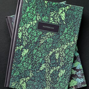 May include: Two notebooks with a green and black leafy pattern. The top notebook has the word "NOTEBOOK" printed on the front cover.