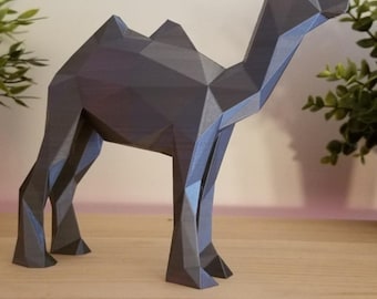 May include: A geometric, gray camel sculpture with a polygonal design. The camel is standing on a wooden surface, with greenery in the background. The sculpture has two humps and is a decorative item.