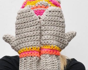 May include: A pair of oversized, hand-knitted mittens and a matching hat. The mittens are light gray with bands of yellow, pink, and orange. The hat features the same colors. The mittens are large enough to cover the face.