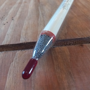 May include: A glass fishing bobber with a red tip and a clear body filled with small silver beads.