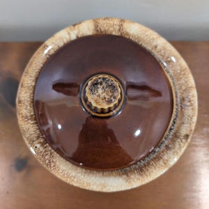 以下が含まれることがあります： 光沢のある仕上がりの茶色のセラミック蓋。蓋は円形で、明るい茶色の縁と、中央にテクスチャ加工されたタン色のノブが付いています。蓋はキャセロール皿または同様のキッチン用品用であるようです。