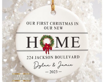 May include: White ceramic Christmas ornament with black text that reads "Our First Christmas in Our New Home" with a wreath and red bow in the center of the word "Home". The text "224 Jackson Boulevard Dylan & Jamie - 2023 -" is below the word "Home".
