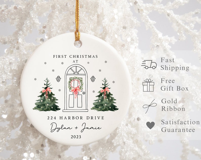 K&ouml;nnte beinhalten: Wei&szlig;er Keramik-Weihnachtsbaumschmuck mit einer handgezeichneten Illustration eines Hauses mit einem Kranz an der T&uuml;r und zwei Weihnachtsb&auml;umen. Der Anh&auml;nger tr&auml;gt die Aufschrift "First Christmas at 224 Harbor Drive Dylan + Jamie 2023".