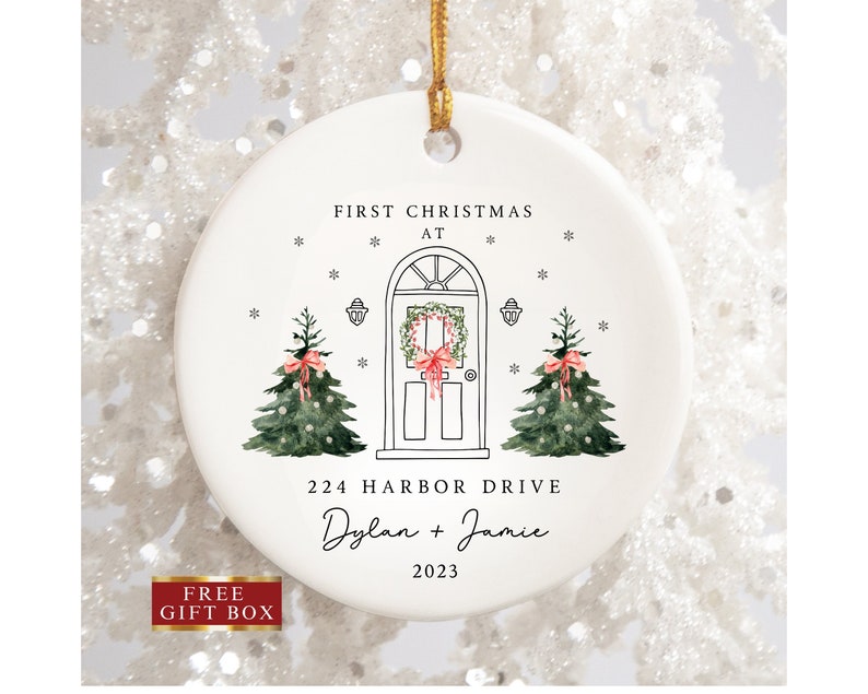 K&ouml;nnte beinhalten: Wei&szlig;er Keramik-Weihnachtsbaumschmuck mit einer handgezeichneten Illustration eines Hauses mit einem Kranz an der T&uuml;r, zwei Weihnachtsb&auml;umen und dem Text "First Christmas at 224 Harbor Drive Dylan + Jamie 2023".