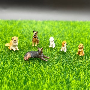 Könnte beinhalten: Sechs Miniatur-Hundefiguren in verschiedenen Posen und Farben, darunter Braun, Schwarz, Weiß und Gold, sind auf einer grünen künstlichen Grasfläche ausgestellt.