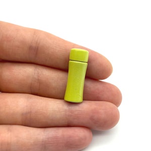 Op de afbeelding: Een kleine, felgele, cilindrische flessenstop. De stop is gemaakt van hout en heeft een gladde, gepolijste afwerking.