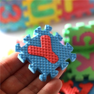 May include: Blue foam puzzle piece with a red letter Y in the center. The puzzle piece has a textured surface.