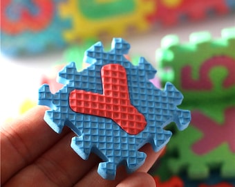 Puede incluir: Pieza de rompecabezas de espuma azul con una letra Y roja en el centro. La pieza del rompecabezas tiene una superficie texturizada.