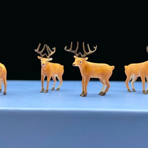 Puede incluir: Cuatro figuritas de ciervo en miniatura con cuerpos marrones y cuernos dorados. Los ciervos están de pie sobre una superficie azul claro.