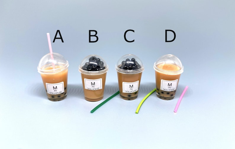 May include: Four miniature plastic cups filled with brown liquid and black boba pearls. Each cup has a clear lid and a white label that reads "M in Dollhouse". The cups are arranged in a row from left to right, with a pink straw in the first cup, a green straw in the second cup, a green straw in the third cup, and a pink straw in the fourth cup.