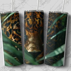 May include: A stainless steel tumbler with a close-up image of a jaguar's face peering through green foliage. The jaguar's fur is brown and black with spots.