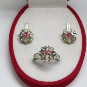 Peut inclure: Un ensemble de bijoux en argent comprenant une bague et des boucles d'oreilles. Chaque pièce présente un motif floral avec une pierre précieuse rose au centre.