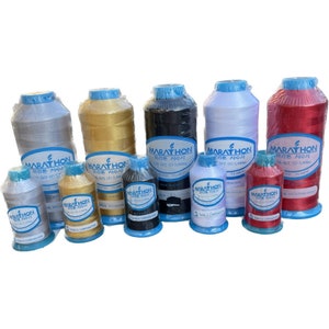 May include: A collection of ten spools of thread in various colours, including silver, gold, black, white, and red. Each spool has a blue label with the text "Marathon" and "미리톤 자수사" in Korean. The spools are arranged in two rows on a white surface.