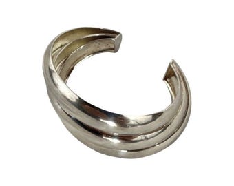 May include: A silver bangle bracelet with a triple-layered design. The bracelet is smooth and polished.