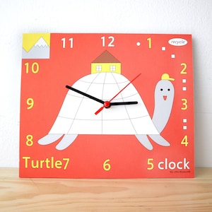 Puede incluir: Un reloj de tortuga rojo y blanco con una casa en su espalda. La esfera del reloj tiene manecillas negras y números amarillos. El reloj dice "Turtle 7" y "5 clock".