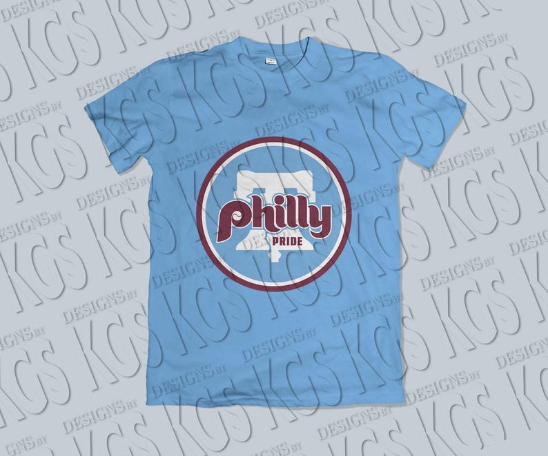 Pode incluir: Camiseta azul claro com um design gr&aacute;fico circular. O design gr&aacute;fico apresenta a palavra "Philly" em escrita bord&ocirc; e as palavras "Pride" abaixo. O design gr&aacute;fico tamb&eacute;m inclui um contorno branco e uma borda bord&ocirc;. A camiseta &eacute; de gola redonda.
