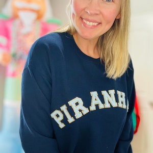 May include: A navy blue sweatshirt with a light blue and gold "PIRANHA" graphic on the front.