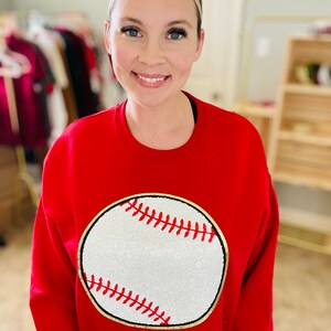 May include: Red sweatshirt with a white baseball graphic with red stitching and a gold outline.