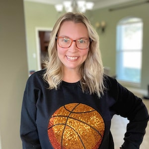 May include: Black sweatshirt with a large sequined basketball design in orange and gold.