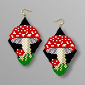 May include: Two diamond-shaped earrings with a red mushroom design and white spots. The earrings have a black background, a beige stem, and green grass at the base. The text "BRICK STITCH PATTERN IN PDF" is at the bottom of the image.