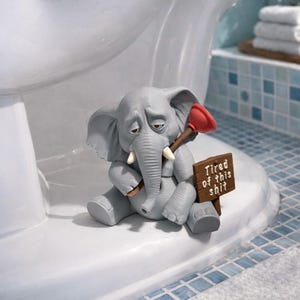 May include: A gray elephant figurine with a sad expression, holding a red plunger and a brown sign that reads "Tired of this shit." The figurine is sitting on a white toilet, with a blue and white tiled background.