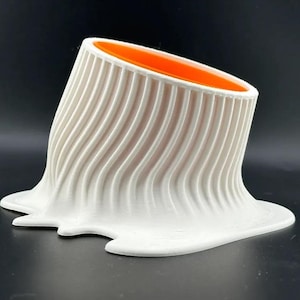 May include: White ceramic vase with a wavy, textured surface and an orange interior. The vase is shaped like a melting object.
