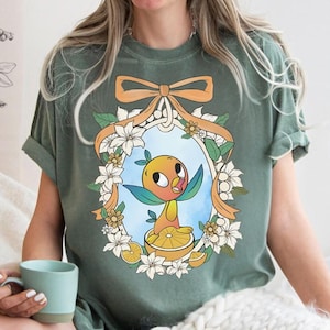 May include: A white ceramic mug with a black handle and the text "But First, Coffee" in a bold, black font. The mug is set against a blurred background, suggesting a cozy setting.