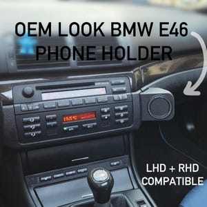 Könnte beinhalten: Ein schwarzer Handyhalter, der am Armaturenbrett eines BMW E46 montiert ist, neben dem Radio und der Klimaanlage. Der Text OEM LOOK BMW E46 PHONE HOLDER und LHD + RHD COMPATIBLE ist auf dem Bild zu sehen.