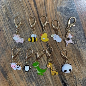 May include: Ten gold-colored metal charms with different animal designs. The charms are attached to a gold-colored metal ring. The animals include a cow, bee, chicken, sheep, pig, penguin, dinosaur, giraffe, and panda.