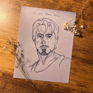 May include: A pencil drawing of a man's face with the text "I am Iron Man..." written above the drawing.